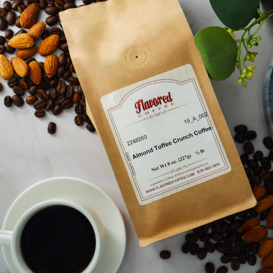Coffee bag labeled 'Almond Toffee Crunch Coffee' with coffee beans and a cup of coffee on a marble surface.