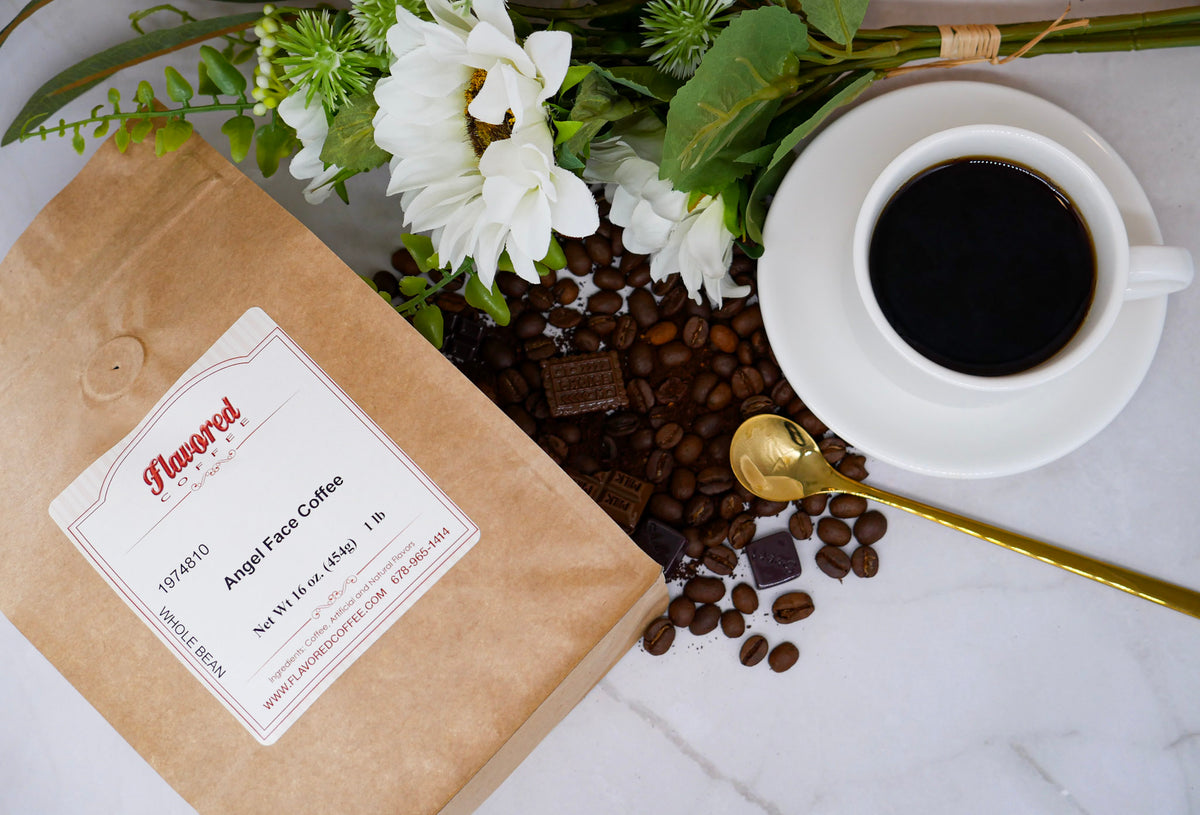 Bag of angel face coffee next to a white mug of coffee, golden spoon, coffee beans and a floral bouquet