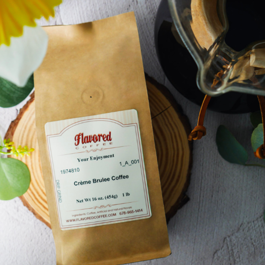 A bag of Flavored Coffee Crème Brulee Coffee in a brown kraft paper package with a white label, styled on a wooden slice coaster and a glass carafe nearby.