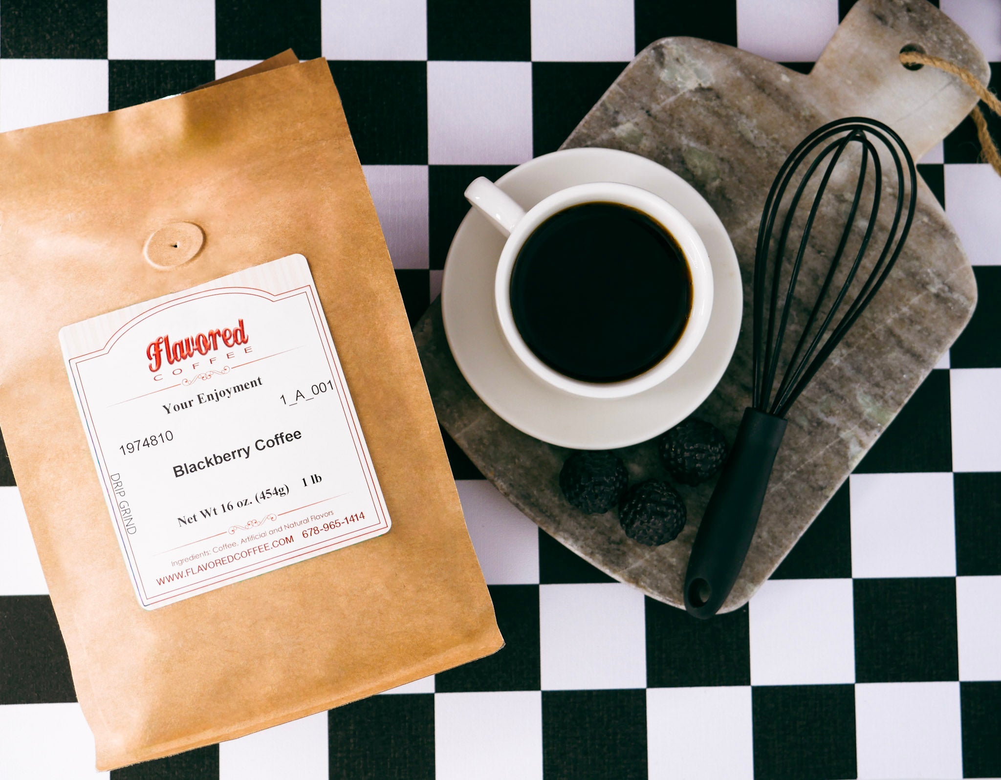 A kraft paper bag of Flavored Coffee Blackberry Coffee is displayed next to a white cup of black coffee on a stone cutting board with a whisk and blackberries, all set on a black and white checkered surface.