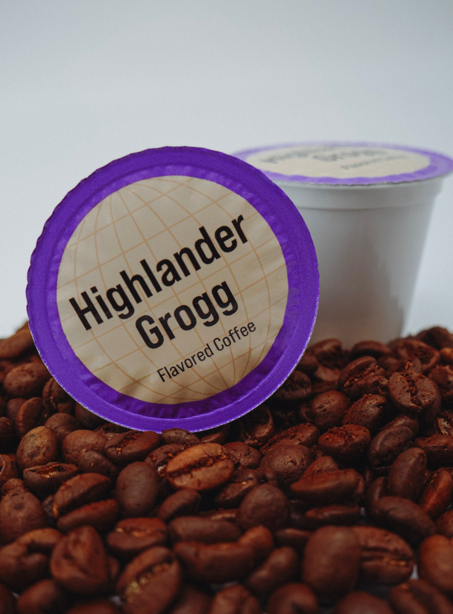 Coffee pod labeled 'Highlander Grogg' on a bed of coffee beans with a white background