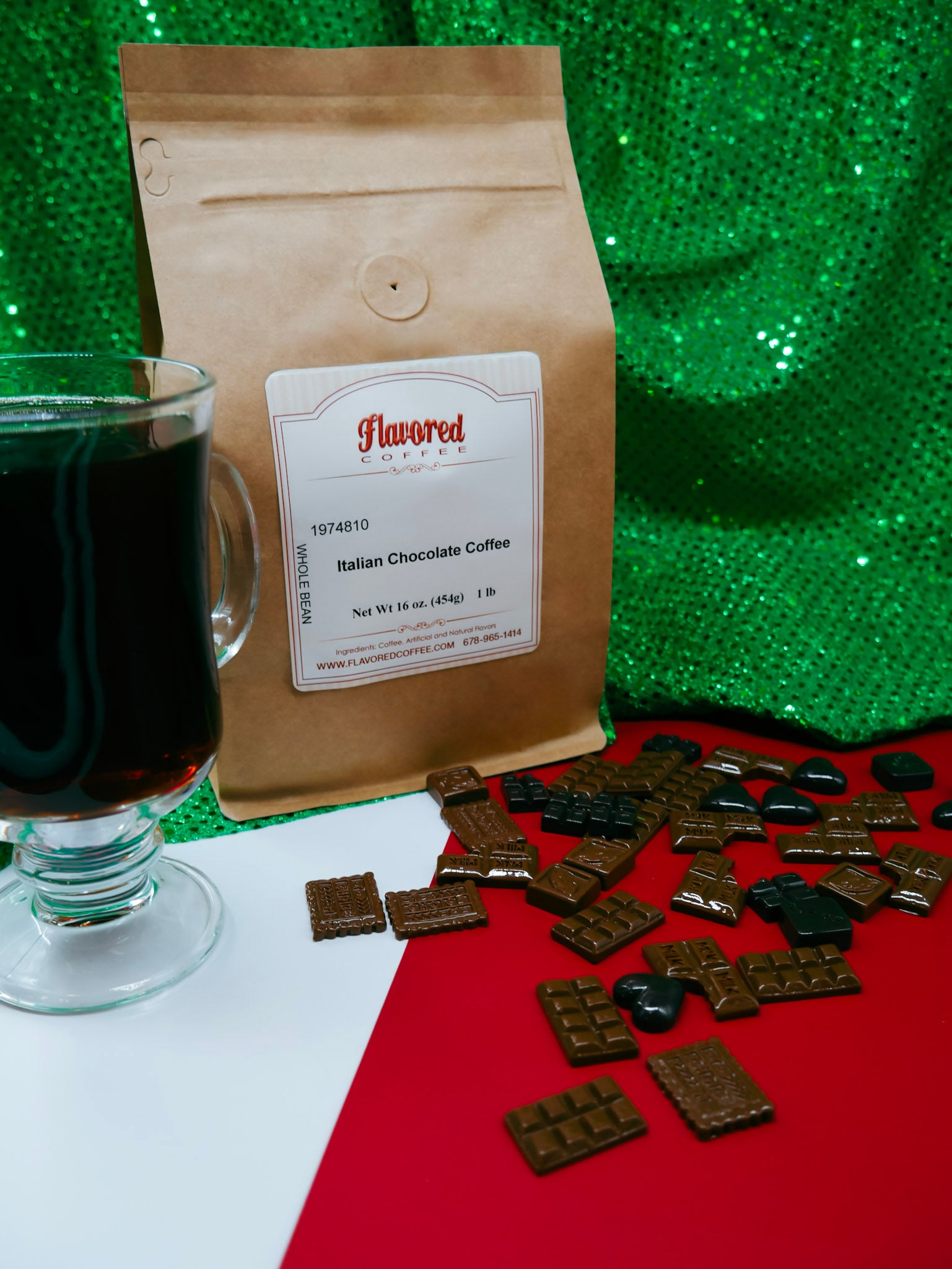 Bag of Italian Chocolate Coffee with a glass of dark liquid and chocolate wafers on a red surface with a green glittery background.