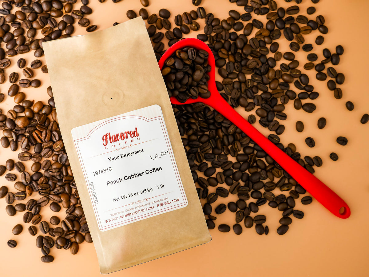 Bag of peach cobbler coffee on a peach colored background with a red coffee scoop and coffee beans